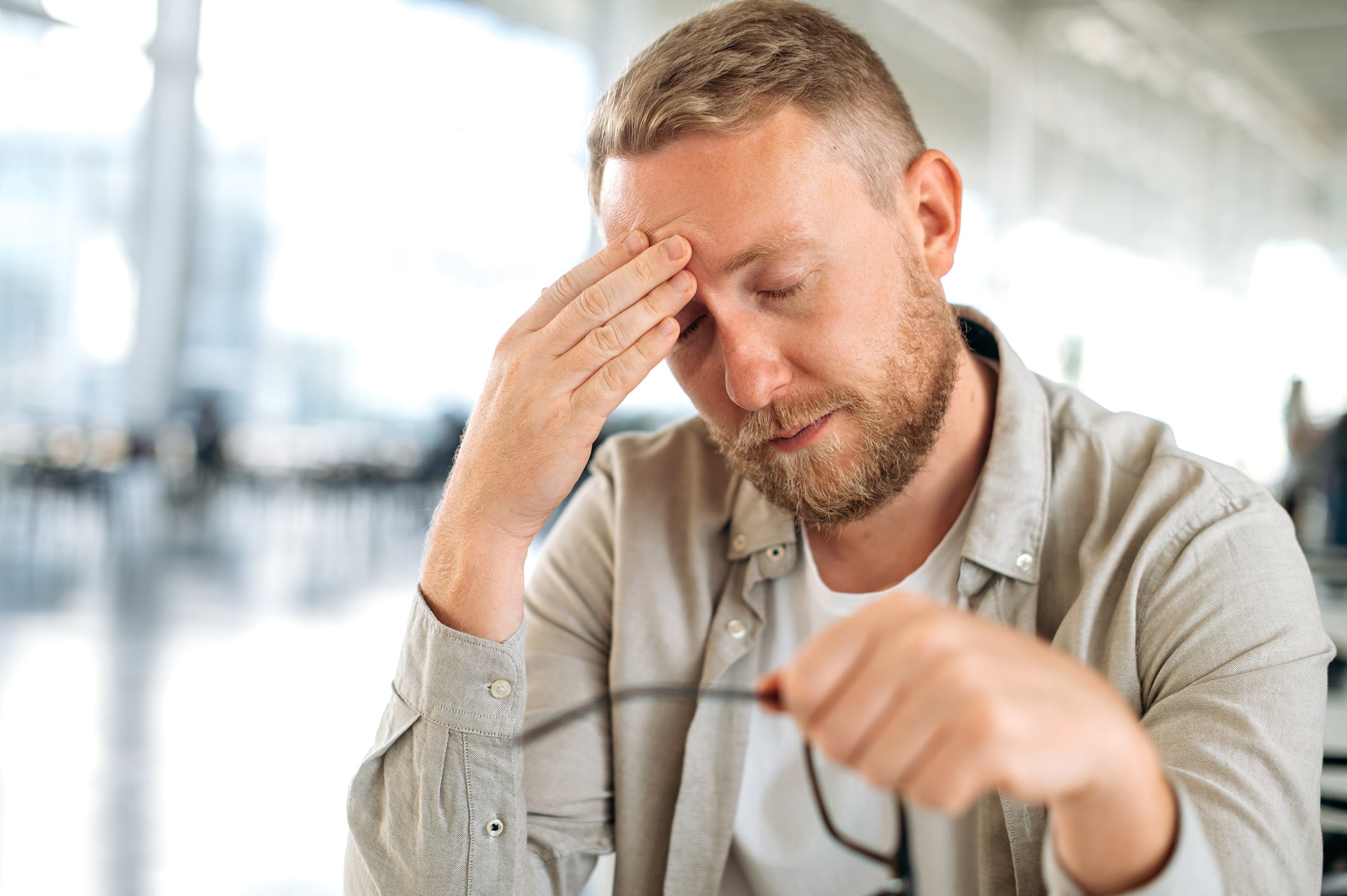 Exhausted caucasian man, company employee, it specialist, sits at the workplace, took off his glasses, closed his eyes, tired from work, feels overtired, has a headache, need a rest or coffee brake